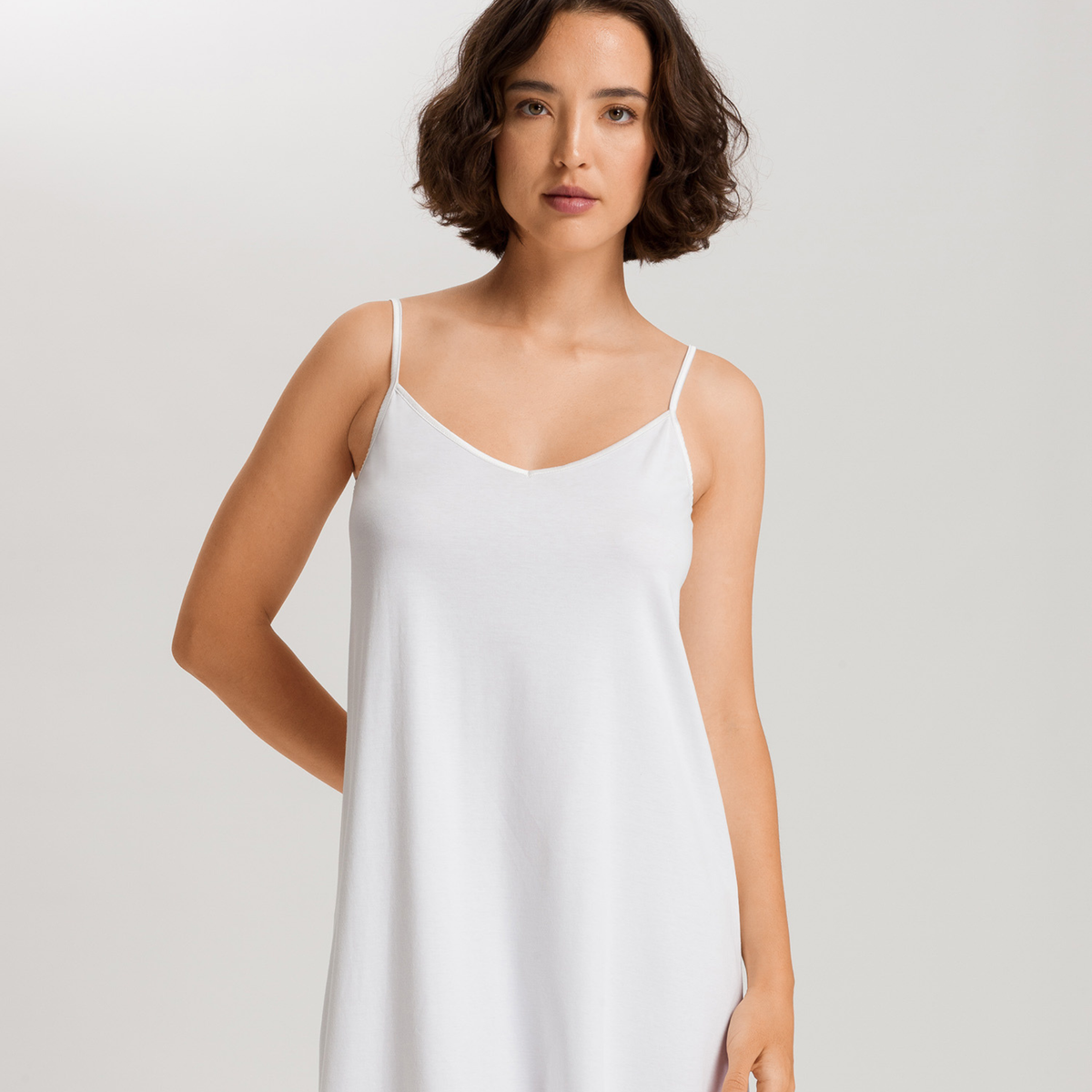 Woman wearing a white slip dress against a plain background