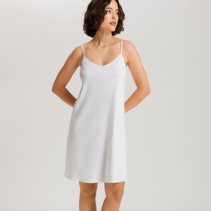 Woman wearing a white slip dress against a plain background