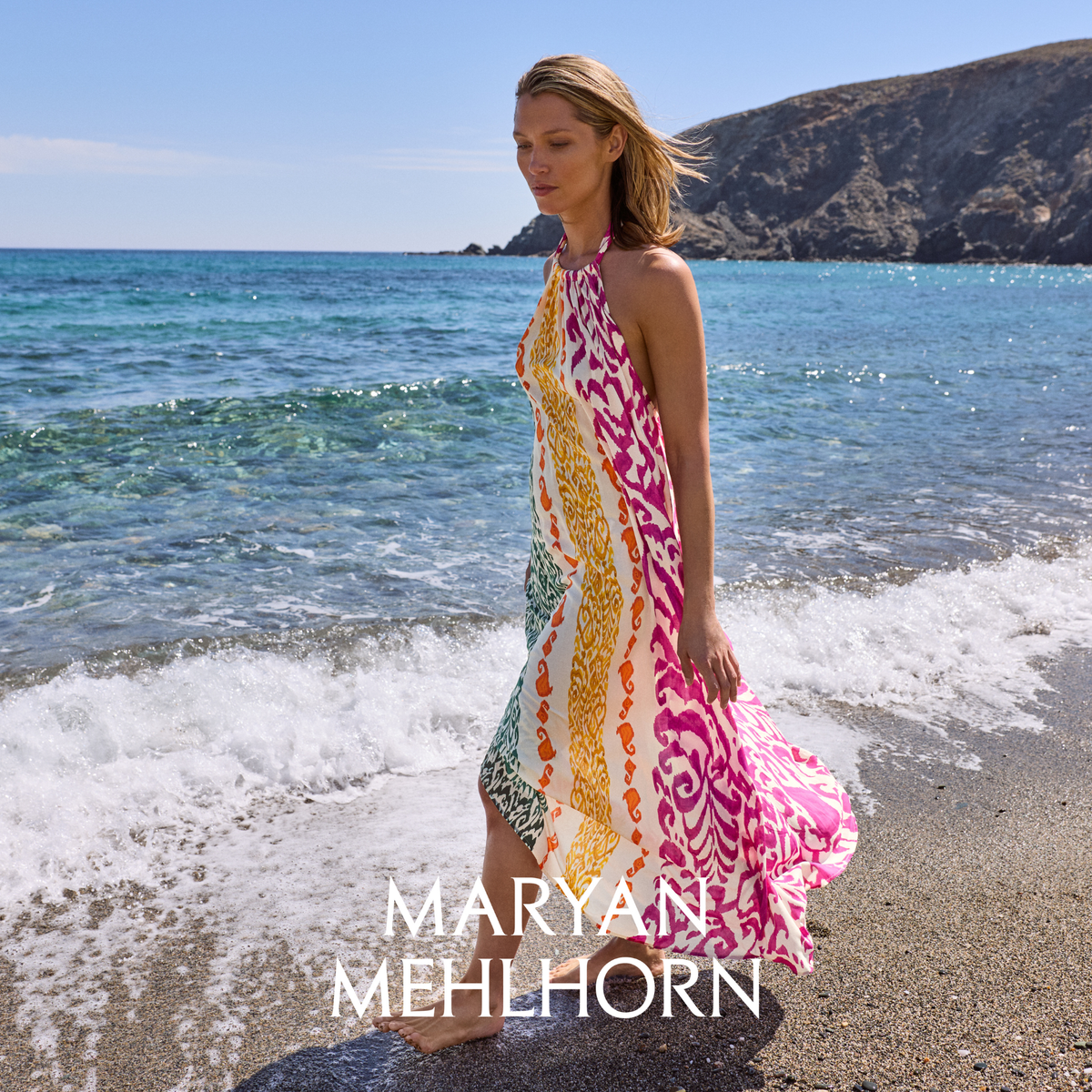 Woman in a colorful dress standing on a beach with 'Maryan Mehlhorn' branding.