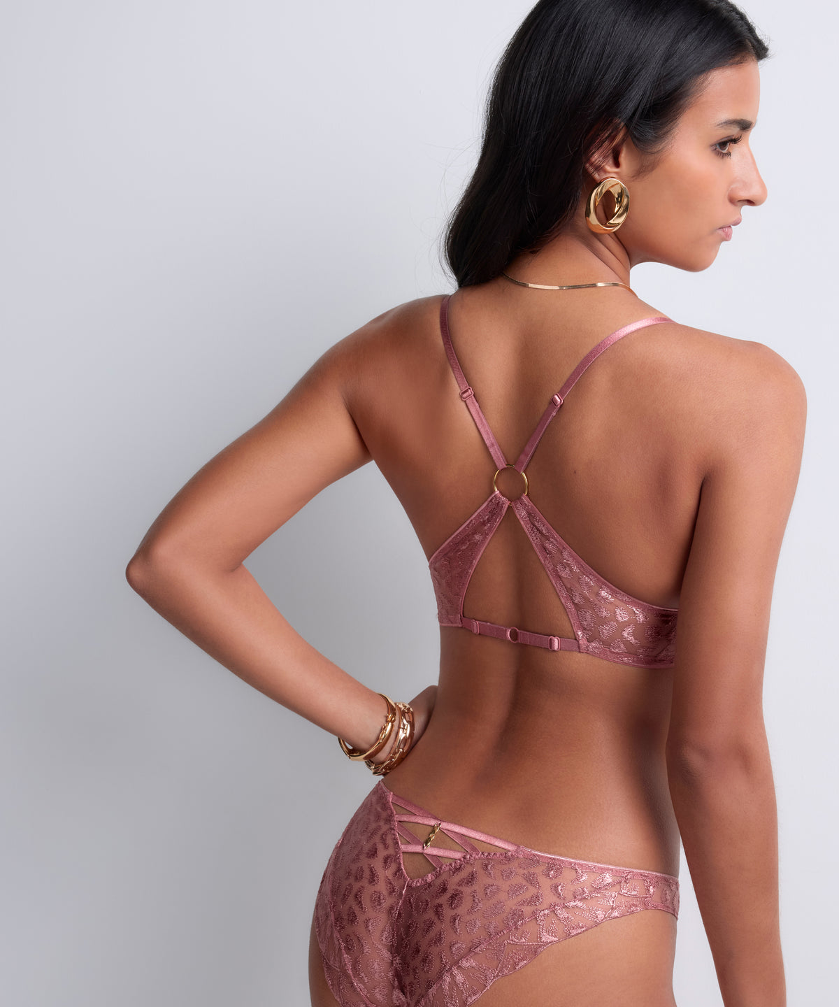 Woman wearing a pink lace lingerie set on a plain background