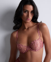 Woman wearing a pink lace bra against a plain background