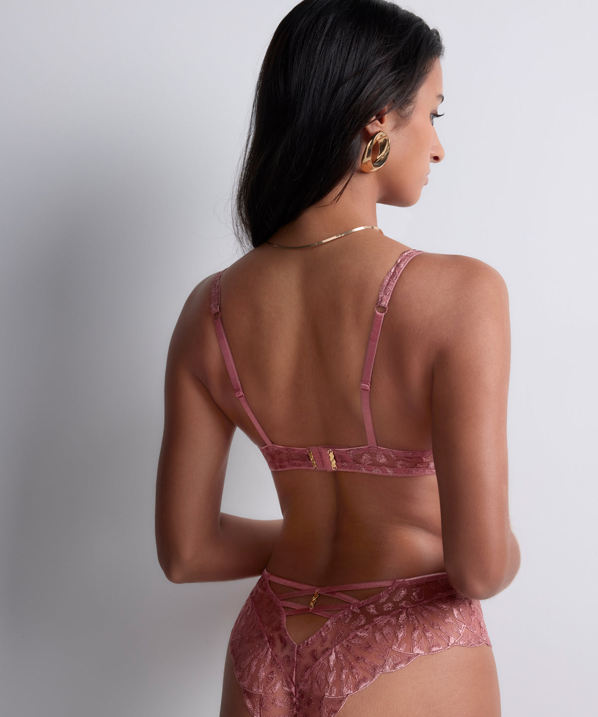 Woman wearing a pink lace lingerie set against a plain background