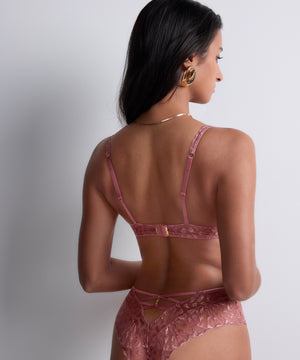 Woman wearing a pink lace lingerie set against a plain background