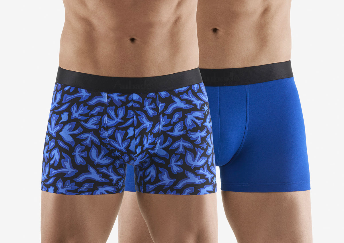 Two pairs of blue boxer briefs, one with a pattern and one solid, on a white background.