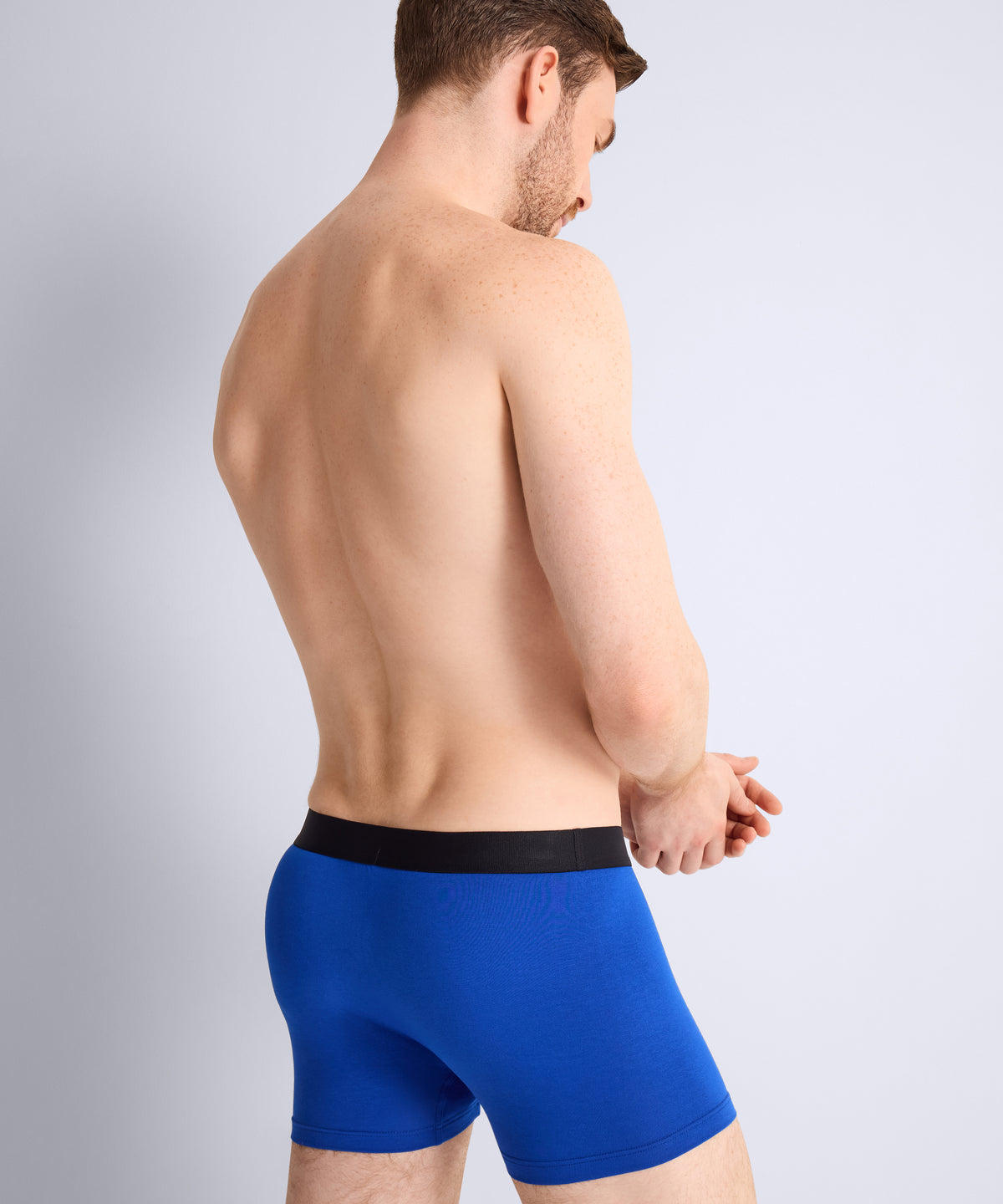Man wearing blue boxer briefs with a black waistband on a light gray background