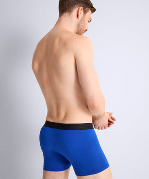 Man wearing blue boxer briefs with a black waistband on a light gray background