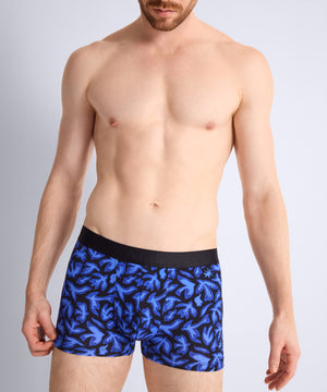 Man wearing blue patterned boxer briefs with a black waistband on a gray background