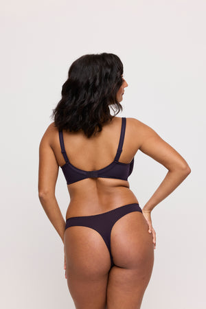 Woman wearing a dark purple lingerie set on a plain background